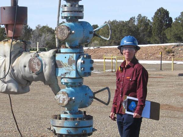 Tracy wearing a hard hat and safety glasses while standing near machinery. 