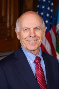 Stevan Pearce wearing a suit in front of a U.S. Flag