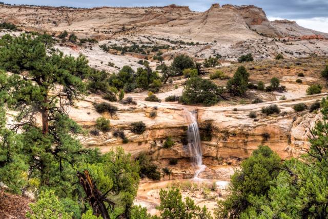 waterfall coming off rocky cliff with slickrock in background
