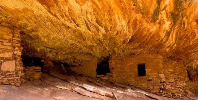 Ancient cliff dwellings built into a rocky overhang with stone walls and small rectangular windows.