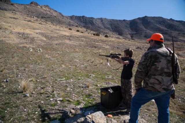 boy shooting at a target with man watching