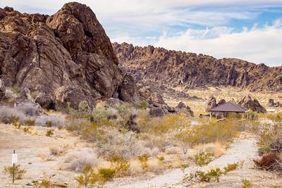A desert campground with shade ramadas under a steep canyon wall.