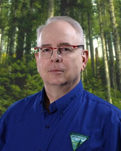 person with short hair wearing a collared shirt posing in front of trees