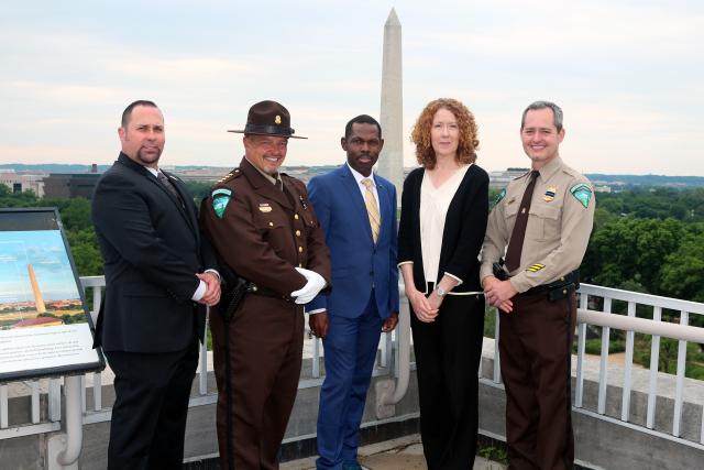 Five people stand on top of a building with the Washington Monument in the background. 
