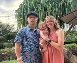 two people, one in a blue shirt and another in a pink dress, holding a baby