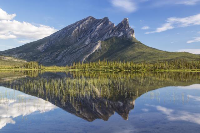 The jagged ridge of Sukakpak Mountain is reflected in the still water of a lake. 