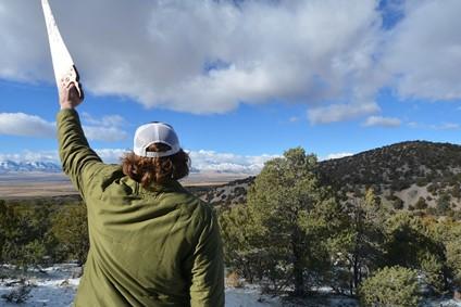 A BLM employee seeks a holiday tree in Silverado Canyon. The subject is holding up a harvesting tool in the air.