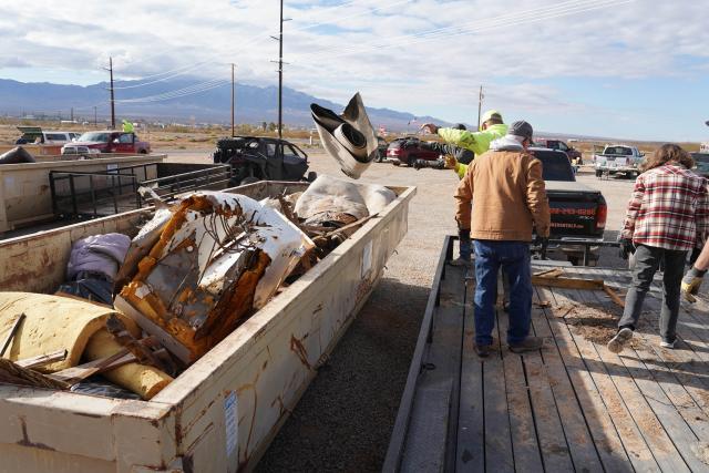 Volunteers fill a large roll-off dumpster with a growing pile of trash.