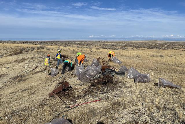 Several people are removing large garbage items from an open, brushy area.