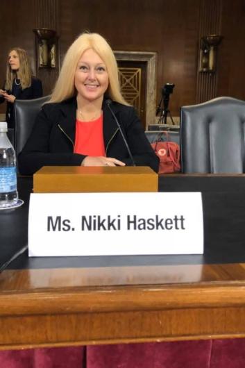 A woman faces the camera and smiles while seated at a table. In front of her is a plaque that reads “Ms. Nikki Haskett.” 