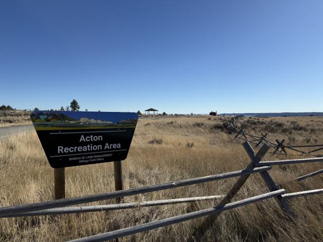 entrance sign for Acton Recreation Area with open grass field and fencing in the background