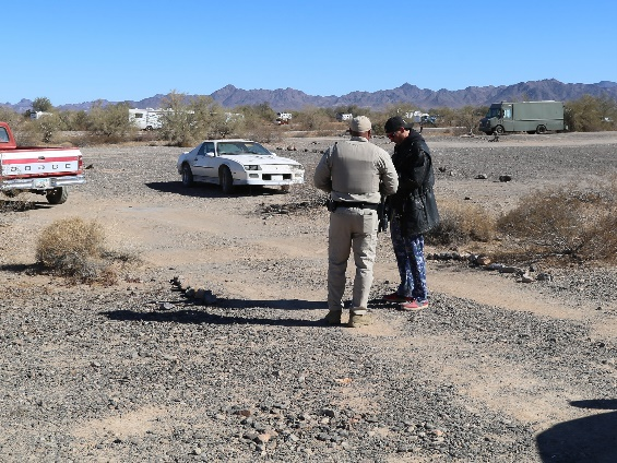 A Ranger stands next to a man with a few vehicles in the background.