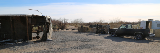 An RV with a hole in it is laying on its side on the left, while several Rangers mill around near a truck on the right. 