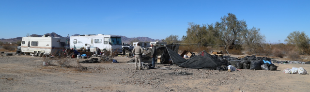 A Ranger stands next to a man with two RVs in the background. 