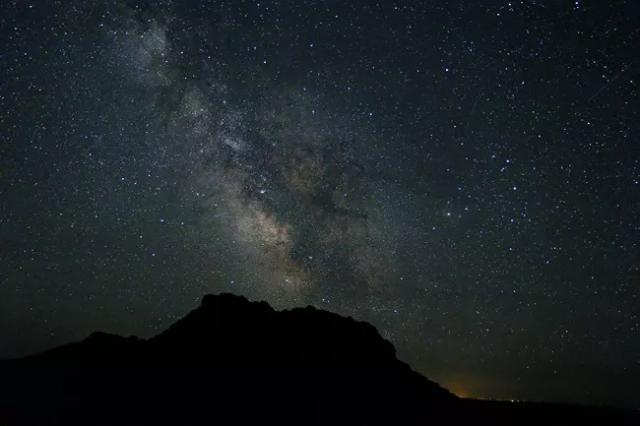 night sky view of milky way with dark silhouette of rocky outcropping below 