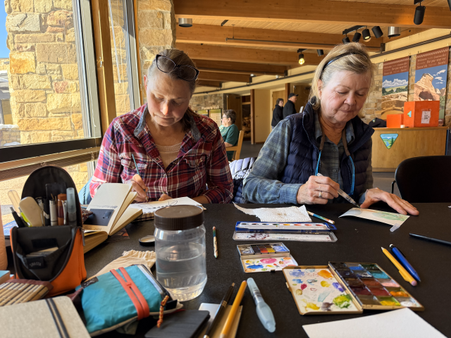 two women paint hearts at a table full of art supplies