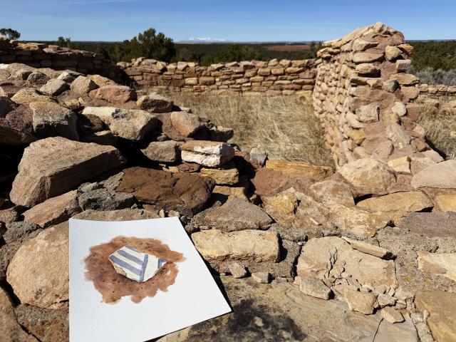 a painting of a black and white pottery sherd rests on the wall of a pueblo