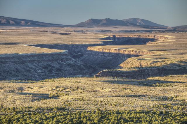 open sagebrush plain and winding gorge with mountains on horizon