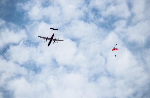 Two people with parachutes drop from an airplane in a blue sky