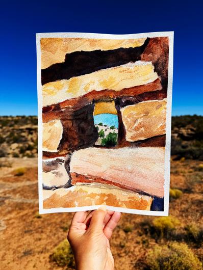 a hand holding a painting in front of a southwest Colorado landscape