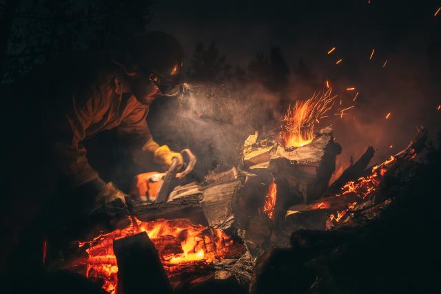 Fire crew member cutting a flaming tree during the night.