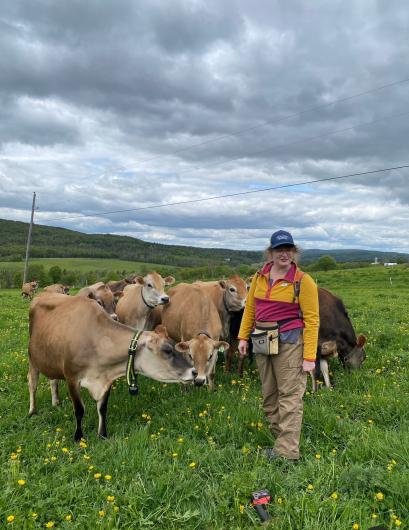 woman stands in grassy field and poses with several brown cows