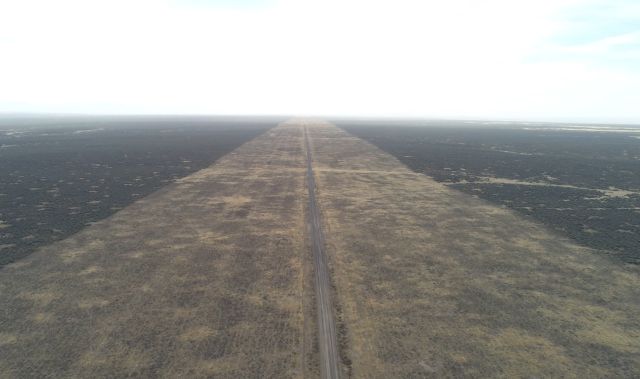 A dirt road in a flat area with a mowed corridor on both sides