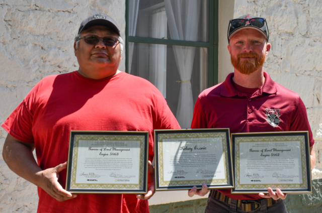 Two men posing with framed certificates