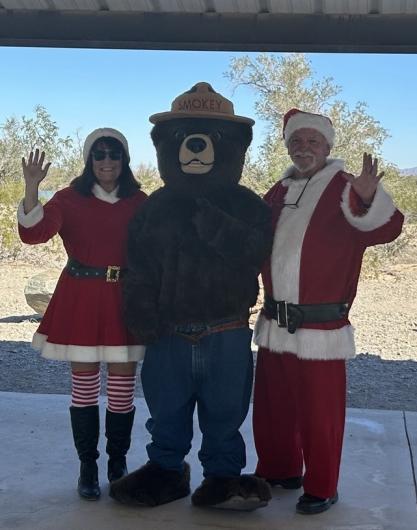 Smokey Bear stands centered between Mrs. Claus and Santa