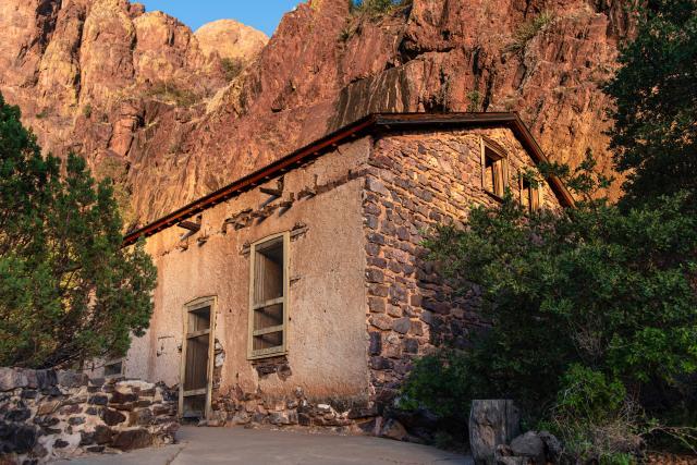 An old stone and concrete building ruin at the base of a rocky cliff.