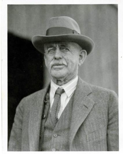 A black and white photo of a man with a mustache wearing a hat and suit