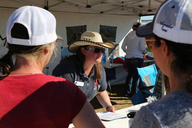 Women in cowboy hat talks to two people at horse adoption event.