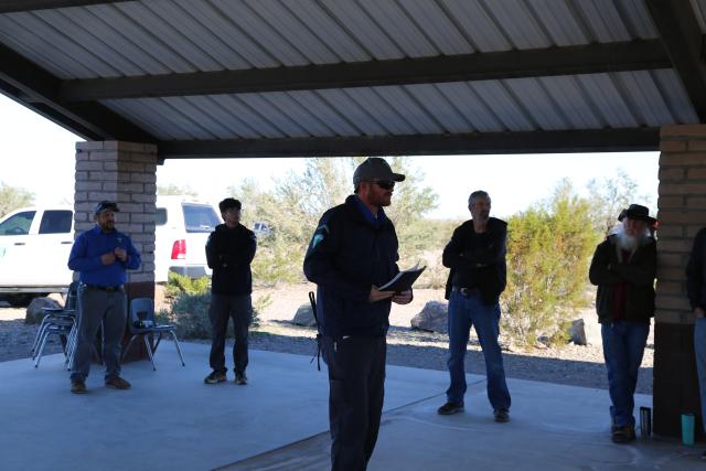 A BLM employee in a dark blue BLM jacket addresses the volunteers gathered while other staff members look on.