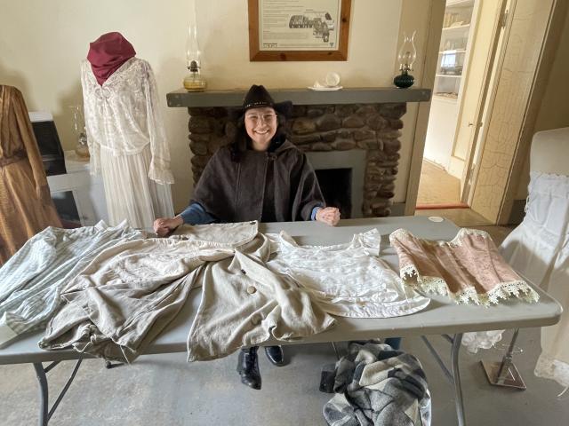  A woman sits behind a display of 19th century clothing