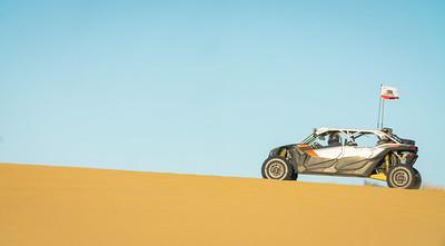 An off road vehicle ascends a gradual dune.