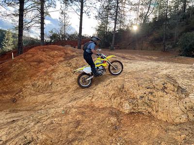 A dirt bike rides up a brown hill in the forest.