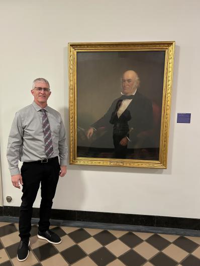 Collin Ewing poses next to a photo of his great-great-great-great-great uncle Thomas Ewing Sr., the first Secretary of the Interior, in the hallway of the Main Interior Building in D.C.