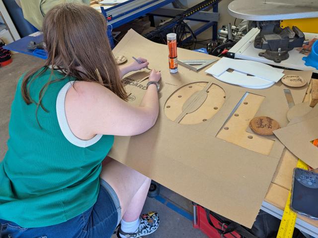 A young woman cuts letters out of a large brown piece of cardboard to make a giant stencil