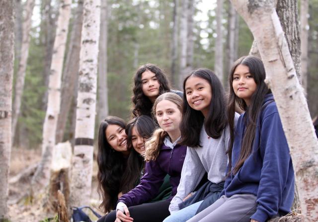Five students smiling and sitting on log.