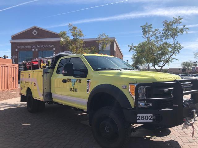 a yellow wildland fire engine sits in front of a brick building with a sign reading Franklin Police and Fire High School