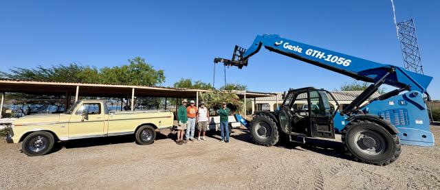 Volunteers stand beside a pickup truck and large telehandler unloading brush for use in fish habitat structures.