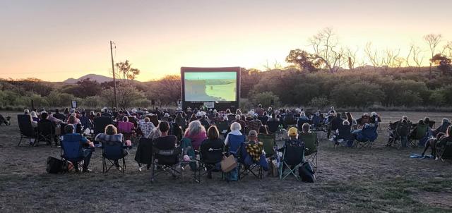 A large group of people in front of an inflatable movie screen outdoors