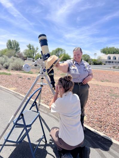 A woman looks through a large telescope on a sunny day