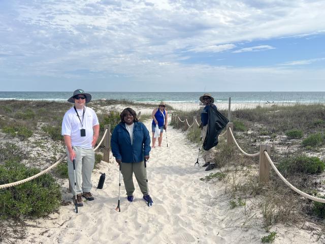 From left to right: Planning and Environmental Specialist, Joe Edmonds; Assistant District Manager, Support Services, Victoria Craft; Administrative Support Assistant, Angela Dennis and Geologist, Samirra Felix work their way along a dune trail, removing debris to support healthy beach ecosystems.