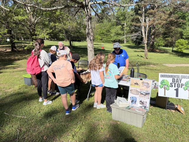 A group of students stand around a table that is covered in animal pelts and archeological artifacts