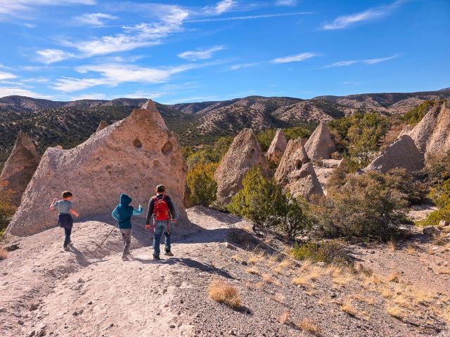 Three people walking next to a large rock along a trail.