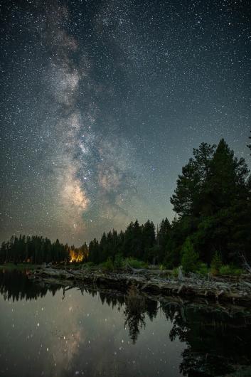 A lake with a camping area near it, at night, under numerous stars.