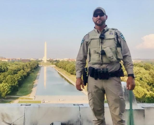A man in uniform stands in front of the National Monument.