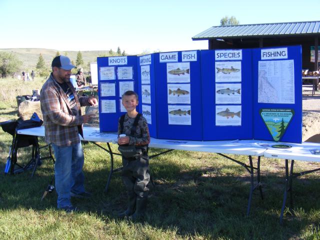 A boy stands dressed all up in fishing gear.