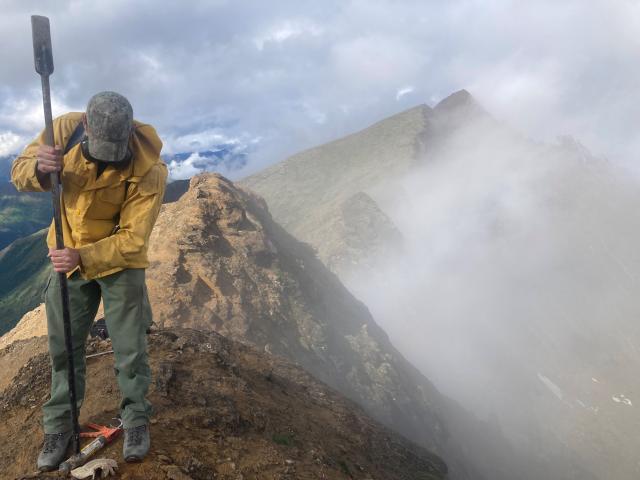 BLM Alaska Surveyor at the top of a steep ridge installing a survey monument for the Ambler Project.